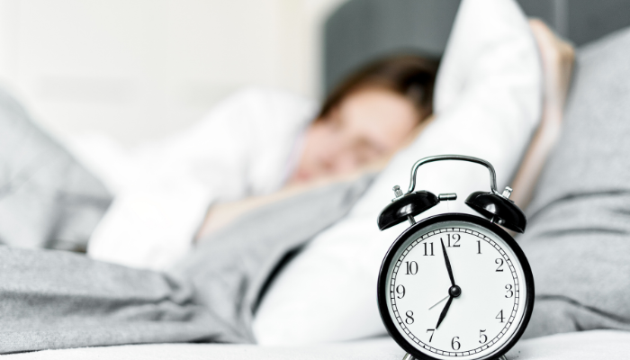Alarm clock with woman asleep in the background 