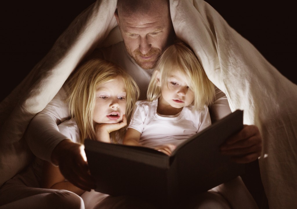 Father and daughters reading book at bedtime