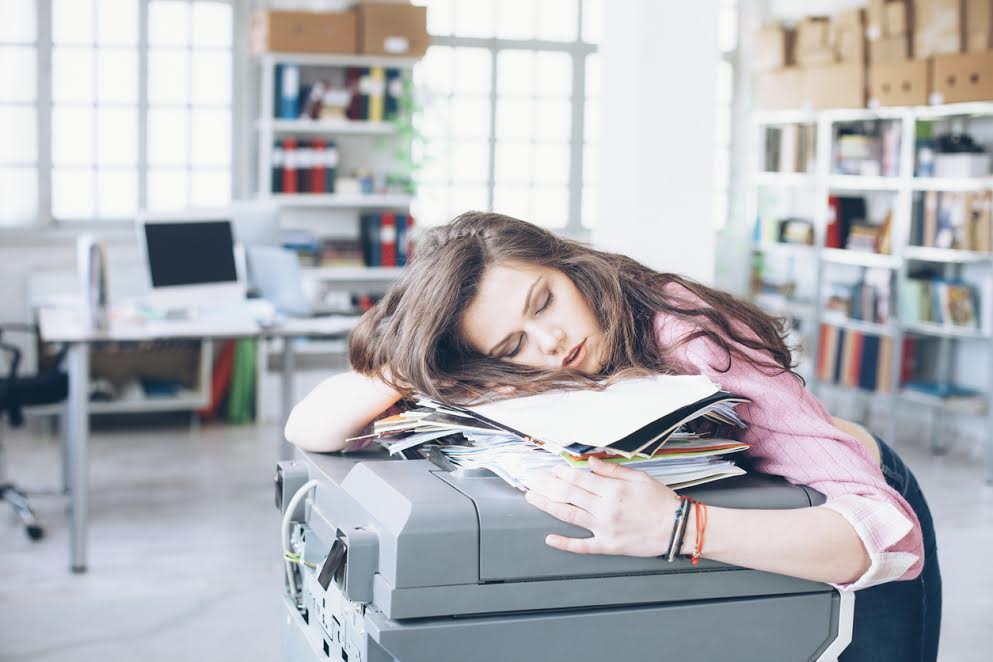 Tired and exhausted young woman sleeping on printer in the office.