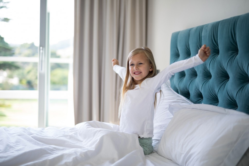 Girl stretching her arms while waking up in bedroom